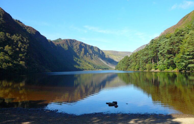 Glendalough upper lake on a beautiful day surrounded by green trees, hilltops and blue sky
