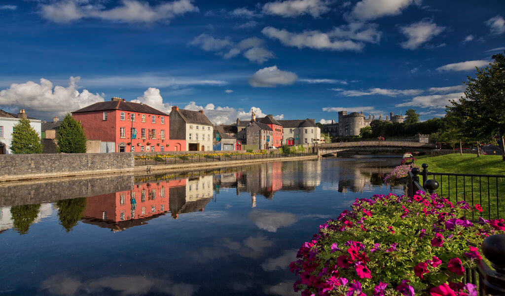 The bank of Kilkenny's river Nore, pretty pink flowers and pink coloured houses with castle in the back